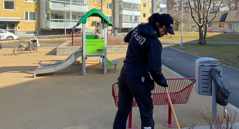 Kvinna i Fabokläder räfsar i en rabatt bredvid en lekplats.