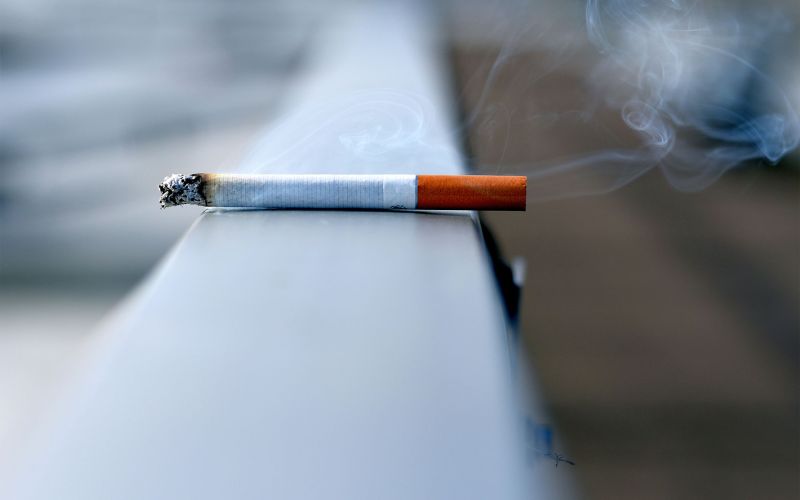 en tänd cigarette ligger på ett balkongsräcke