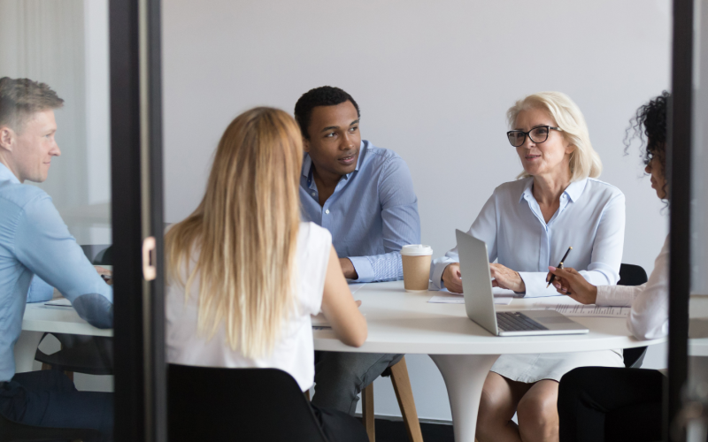 Fem personer sitter runt ett bord - pratar med varandra